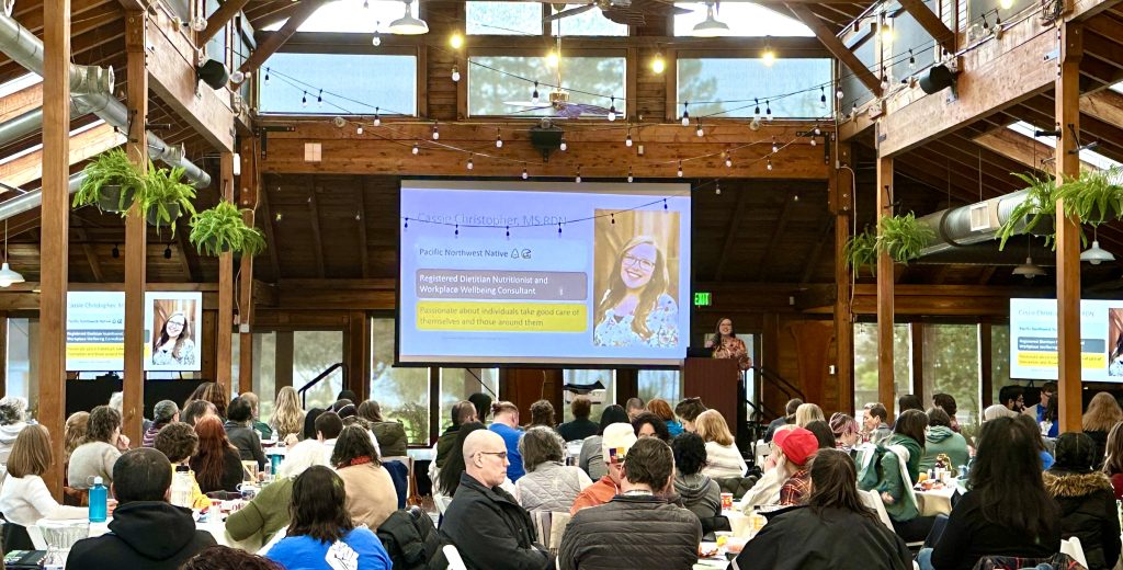Photo of Cassie Christopher presenting a wellness workshop to a crowd of 200+ people